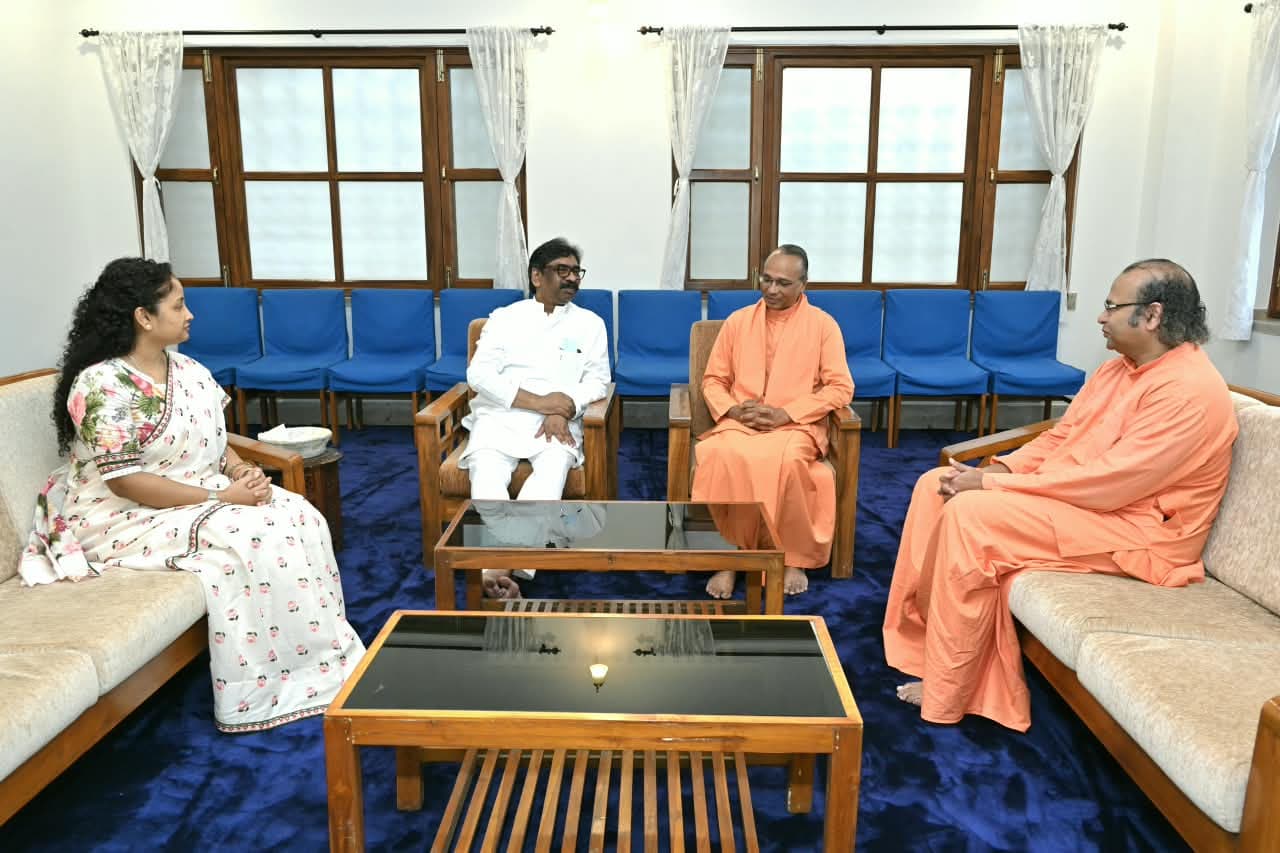 तस्वीर में एक कमरे में सोफे और कुर्सियों पर बैठे चार लोग बातचीत करते दिखाई दे रहे हैं। मुख्यमंत्री हेमंत सोरेन सफेद पोशाक में बैठे हैं, जबकि कल्पना सोरेन सफेद साड़ी में हैं। दोनों ओर भगवा वस्त्र पहने दो संन्यासी बैठे हैं। पीछे नीली कुर्सियां और खिड़कियां दिखाई दे रही हैं।