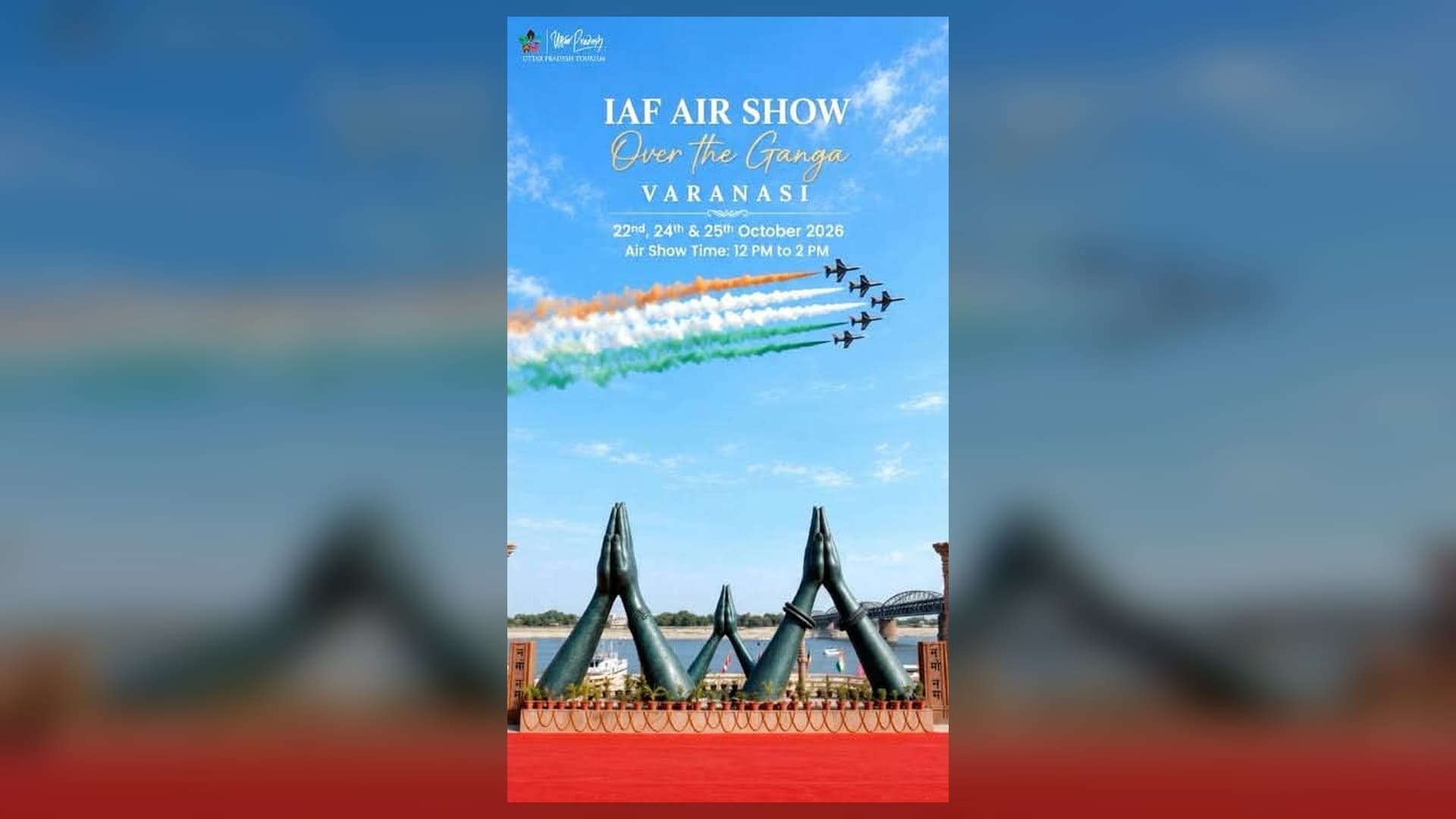 नीले आसमान में पांच विमान पीछे केसरिया, सफेद और हरे रंग का धुआं छोड़ते हुए उड़ रहे हैं। नीचे नदी किनारे हाथ जोड़ने की मुद्रा वाली बड़ी मूर्तियां और पीछे पुल दिखाई दे रहा है। ऊपर "IAF Air Show, Over the Ganga, Varanasi" और तारीखें लिखी हैं।