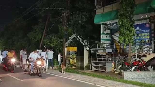 रात के समय निमापाड़ा में एक सड़क के किनारे स्थित इमारत के बाहर कई लोग और दोपहिया वाहन दिखाई दे रहे हैं। इमारत के बाहर एक गेस्ट हाउस/व्यावसायिक परिसर जैसा प्रवेश द्वार और आसपास वाहन खड़े नजर आ रहे हैं।
