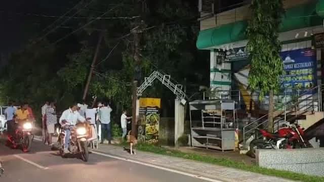 रात के समय निमापाड़ा में एक सड़क के किनारे स्थित इमारत के बाहर कई लोग और दोपहिया वाहन दिखाई दे रहे हैं। इमारत के बाहर एक गेस्ट हाउस/व्यावसायिक परिसर जैसा प्रवेश द्वार और आसपास वाहन खड़े नजर आ रहे हैं।
