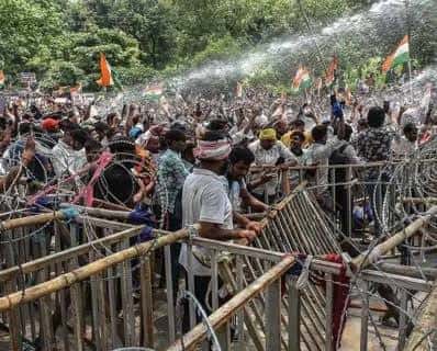 बैरिकेड और कंटीले तारों के पीछे बड़ी संख्या में लोगों की भीड़ दिखाई दे रही है। कई लोगों के हाथों में तिरंगे और केसरिया-हरे झंडे हैं और ऊपर से पानी की बौछार होती दिख रही है।