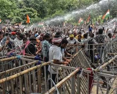 बैरिकेड और कंटीले तारों के पीछे बड़ी संख्या में लोगों की भीड़ दिखाई दे रही है। कई लोगों के हाथों में तिरंगे और केसरिया-हरे झंडे हैं और ऊपर से पानी की बौछार होती दिख रही है।