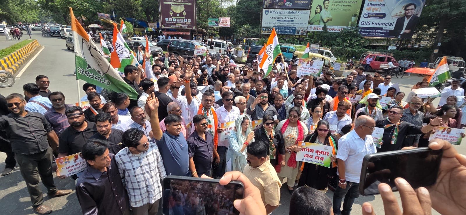 जमशेदपुर में कांग्रेस कार्यकर्ता बड़ी संख्या में सड़क पर मार्च करते दिखाई दे रहे हैं। प्रदर्शन में कांग्रेस के झंडे और बैनर दिखाई दे रहे हैं, जबकि कई कार्यकर्ता हाथ उठाकर नारे लगाते नजर आ रहे हैं। तस्वीर के पीछे सड़क, वाहन और आसपास के व्यावसायिक प्रतिष्ठानों के बोर्ड दिखाई दे रहे हैं।